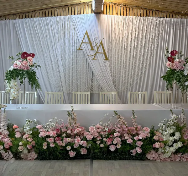 Стол молодожёнов: белая драпировка с монограммой A&A, цветочные стойки и длинная композиция из розовых и белых цветов вдоль стола
